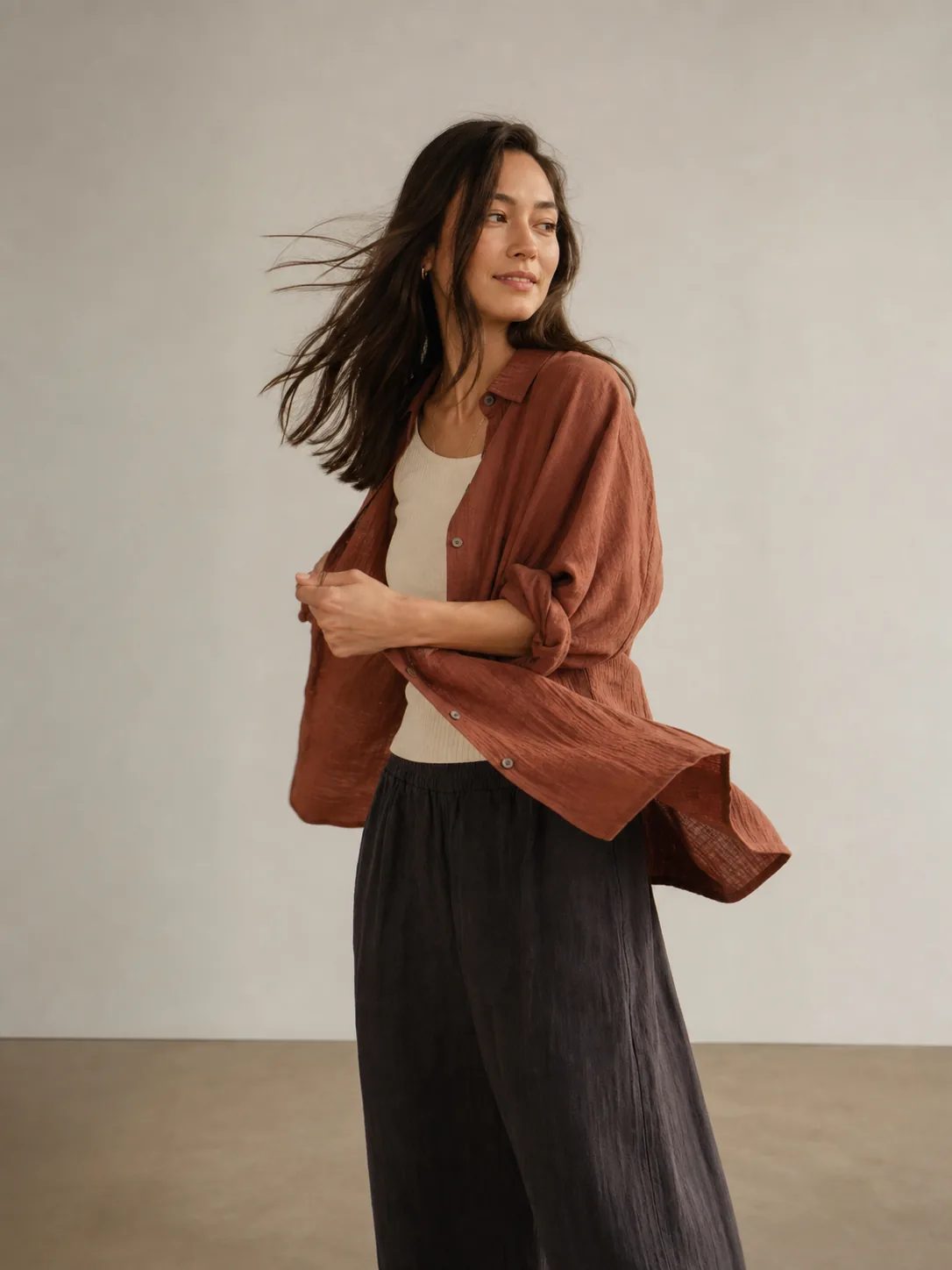 Person turning in a warm studio with her hair and rust-colored overshirt caught in motion
